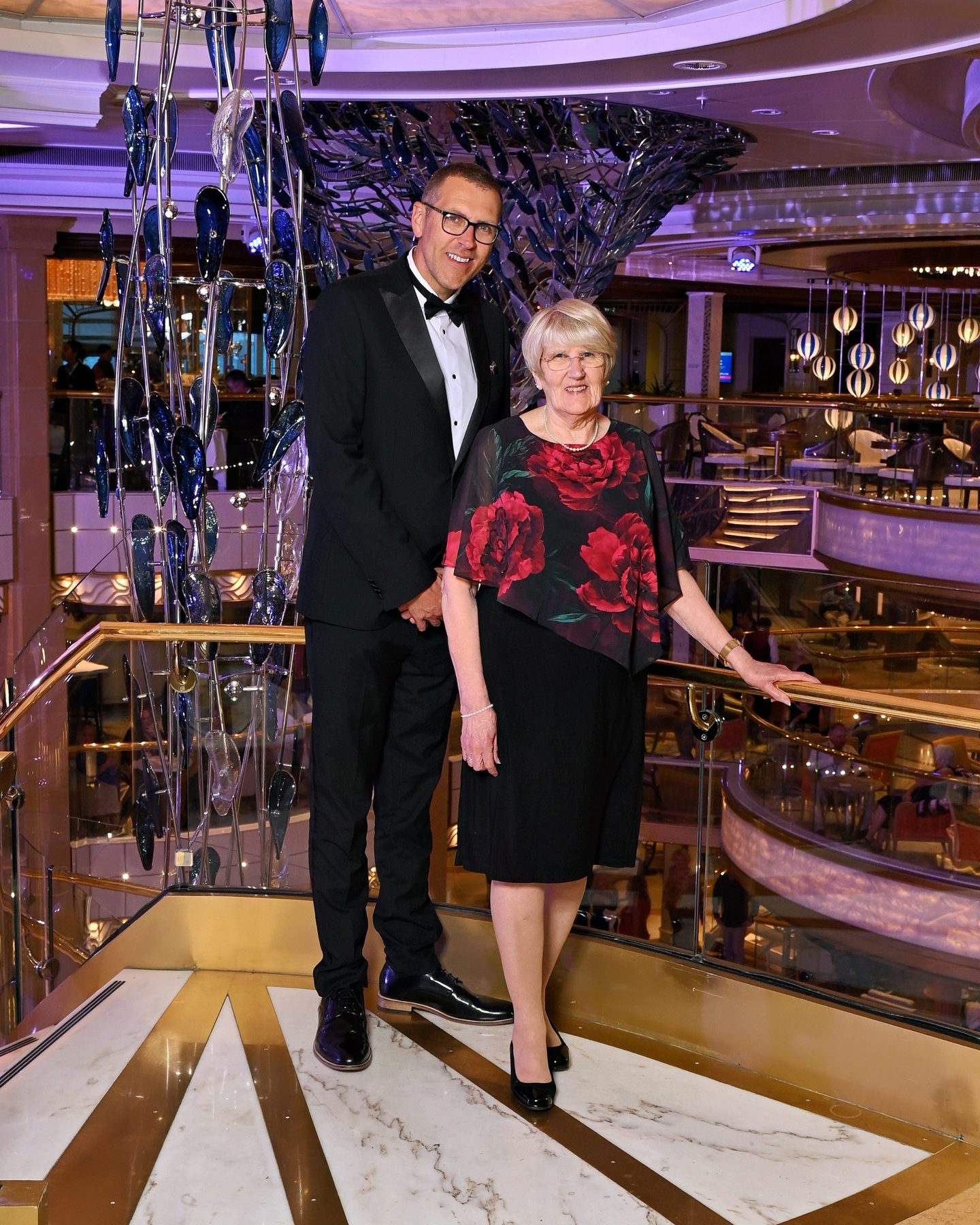Stuart and Frances in formal wear by a chandelier corridor