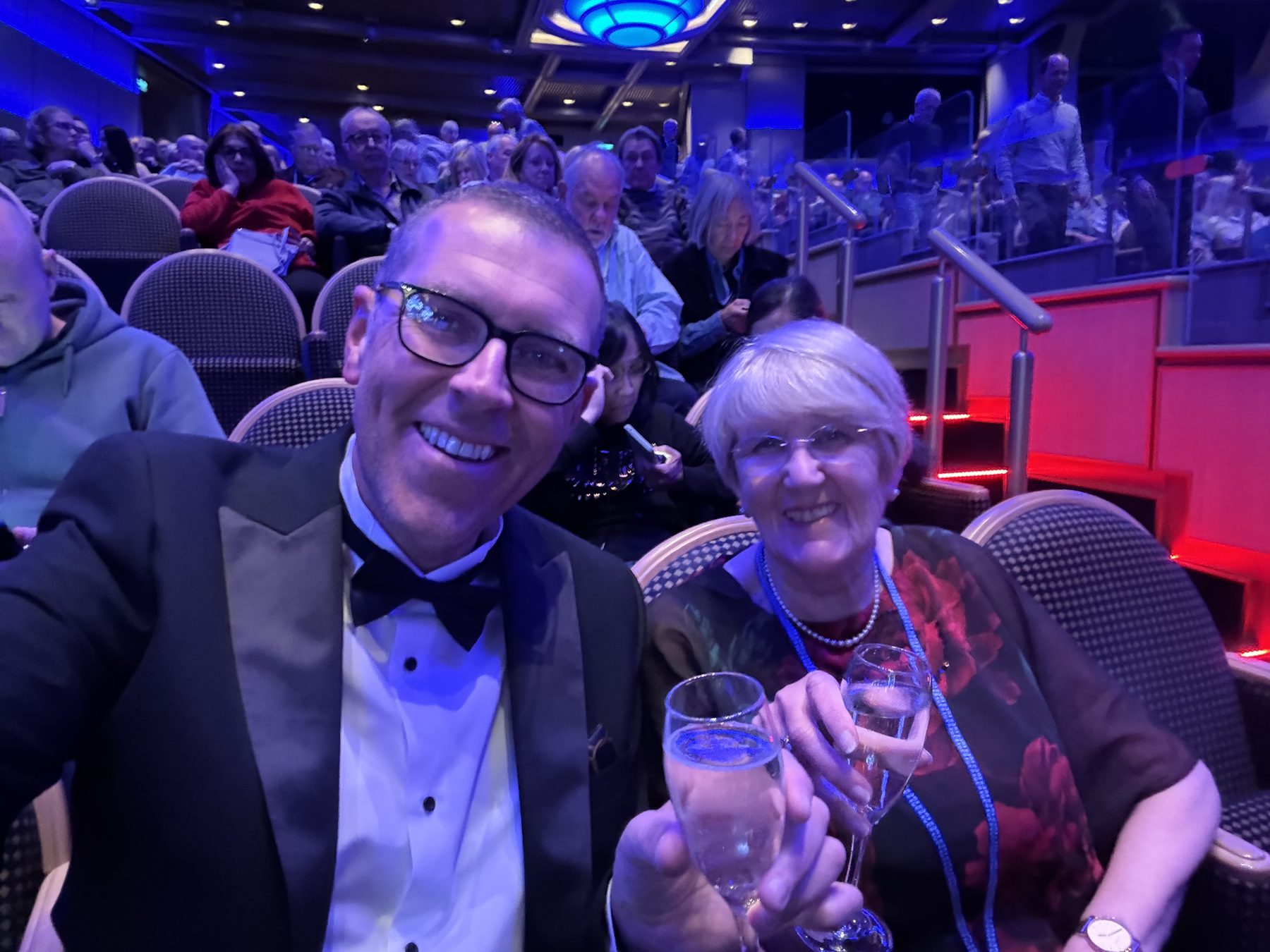 Stuart in tuxedo and Frances in red peony dress with champagne flutes in the theatre
