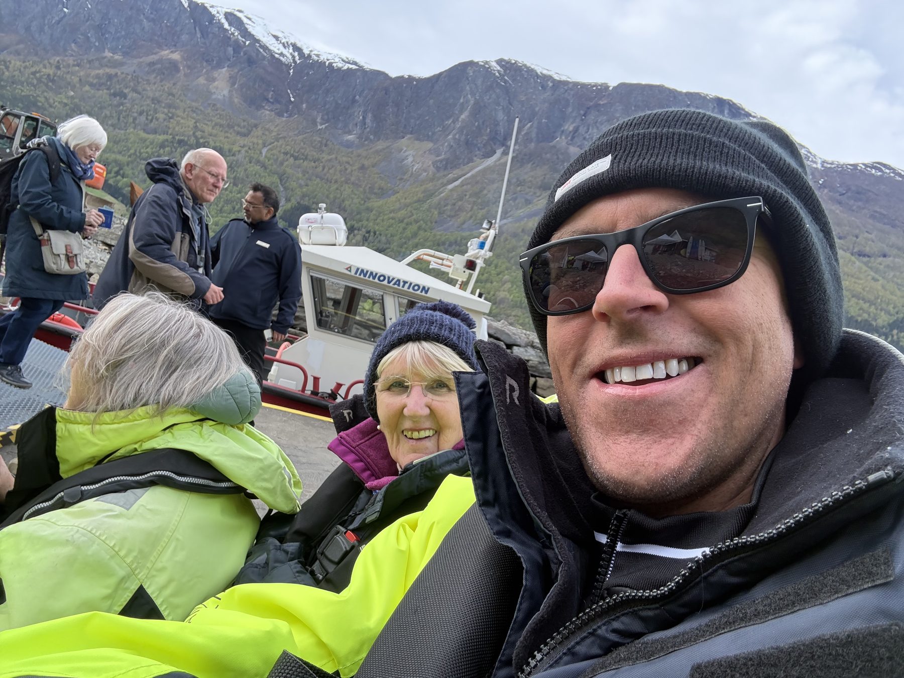 Selfie of Stuart with Frances behind, mountains and INNOVATION boat in background