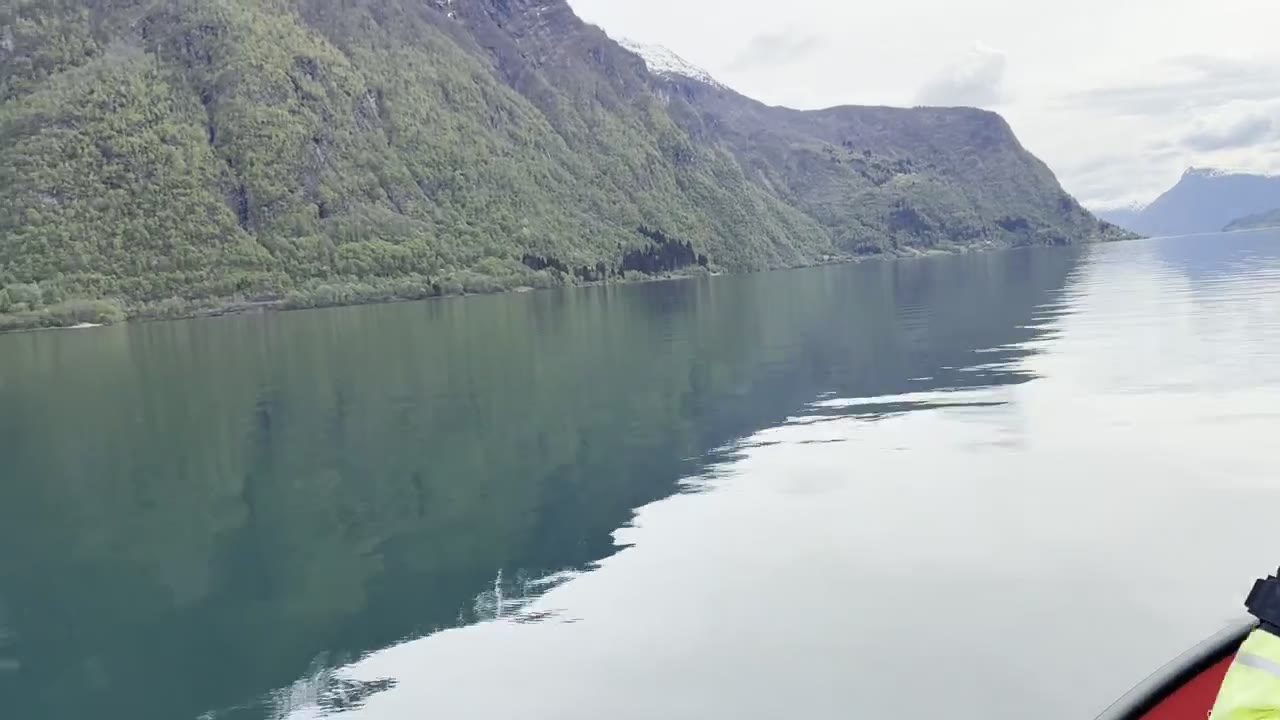 Calm fjord water reflecting the green-and-snow mountains